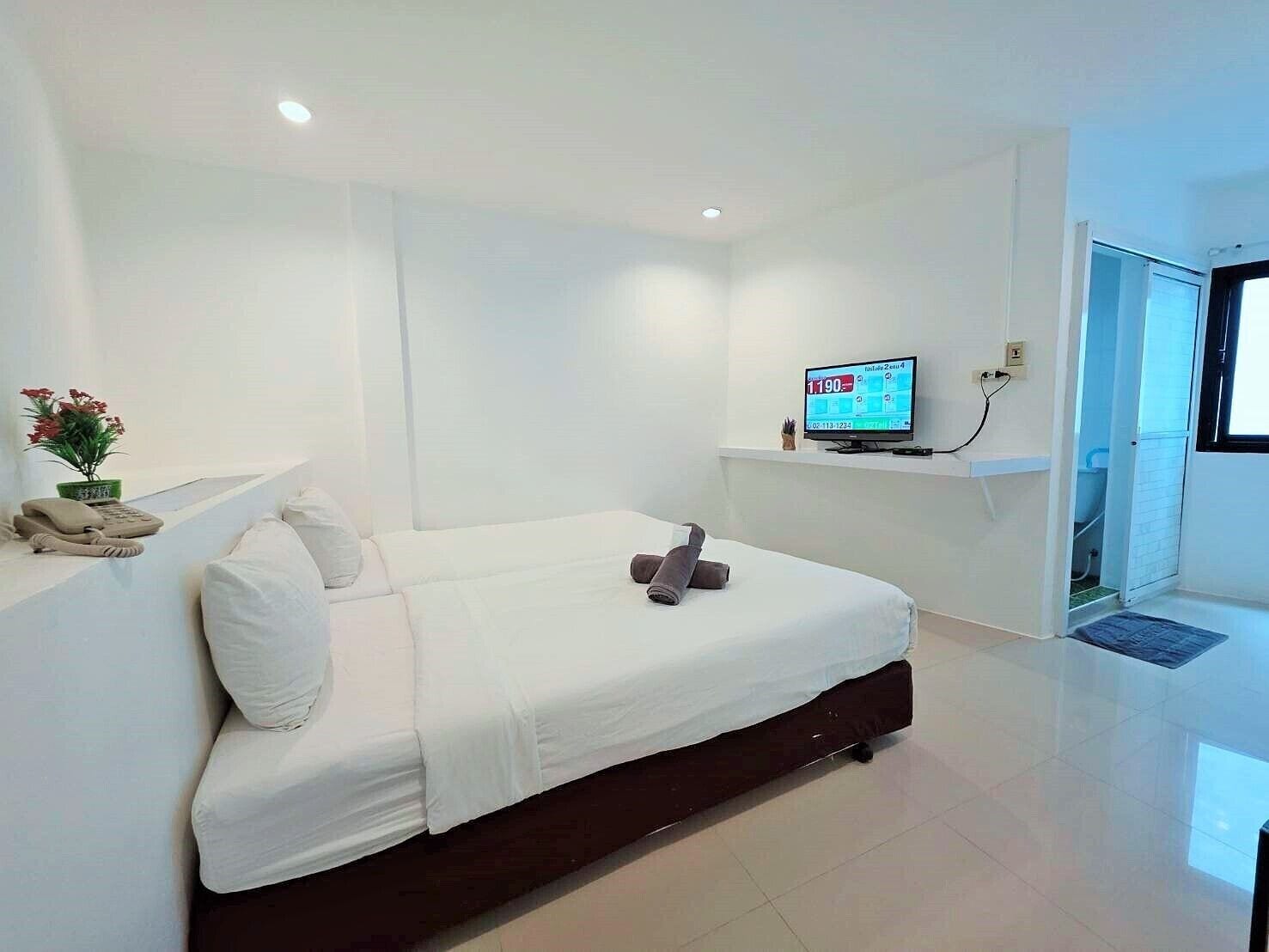 A modern hotel room with a large bed, a flat-screen TV mounted on the wall, and a small desk with a telephone and a plant.
