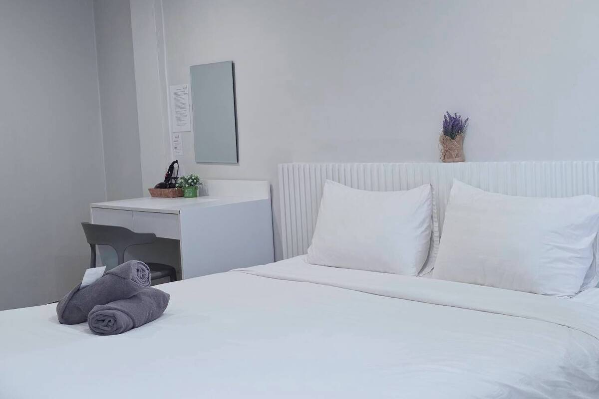 Une chambre d’hôtel avec un lit, un bureau et une chaise. Il y a une petite plante sur le bureau et une serviette sur le lit.