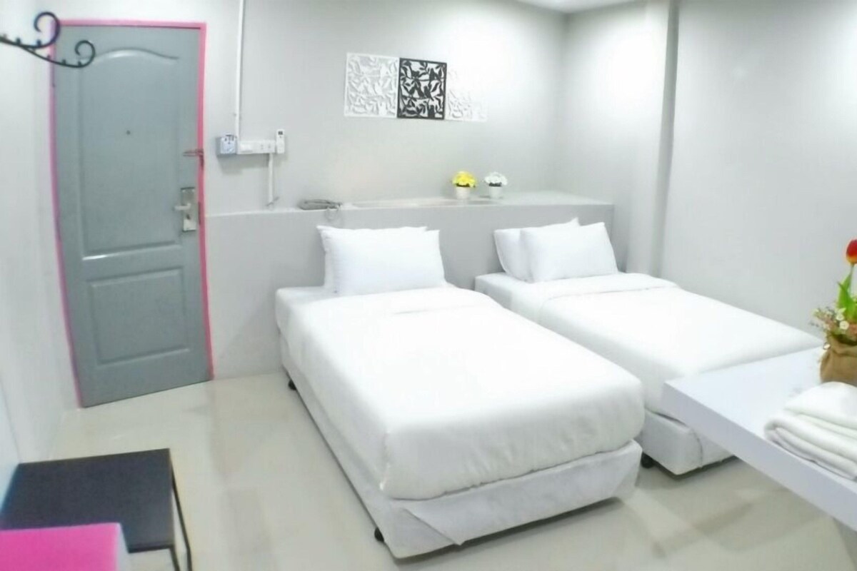 A hotel room with two beds, a desk with a computer, a TV, and a small plant.