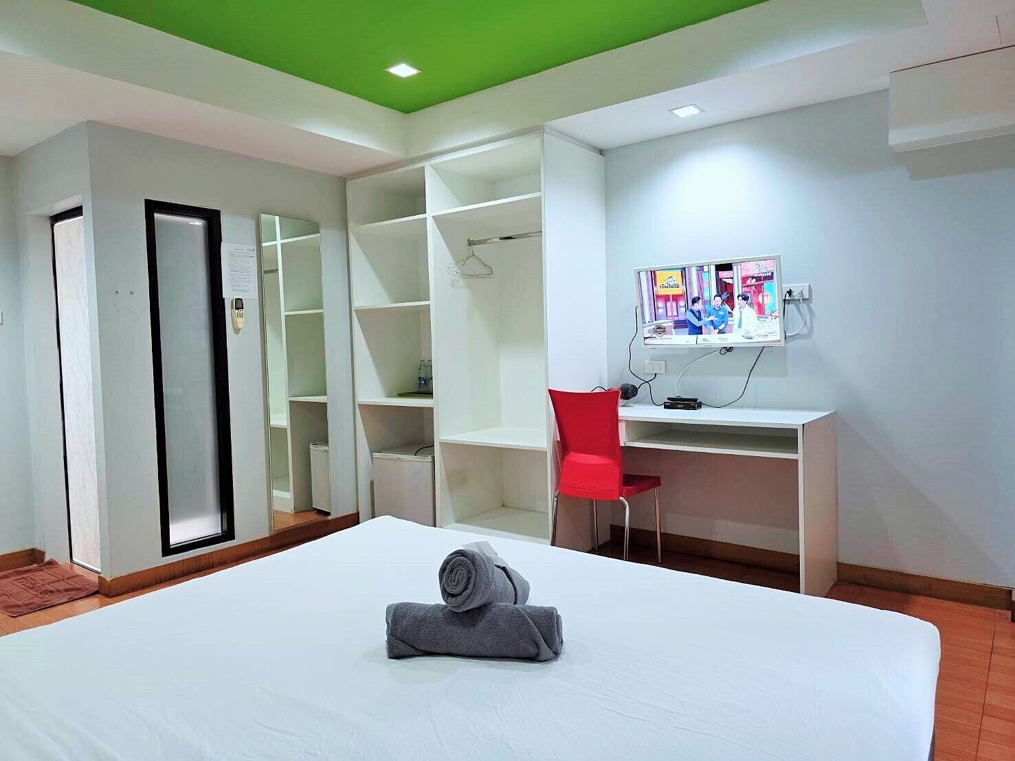 A hotel room with a bed, a desk, a red chair, a wardrobe, and a green ceiling.