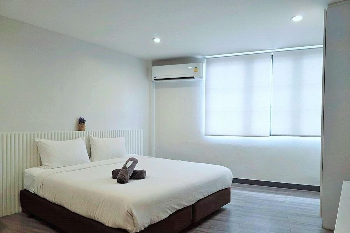 A modern hotel room with a large bed, a radiator, an air conditioning unit, and a window with blinds.