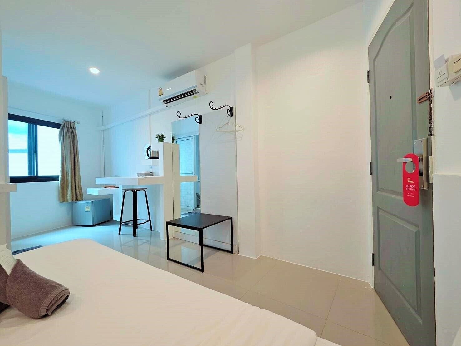 A modern hotel room with a bed, a small desk, a chair, and a window with curtains.