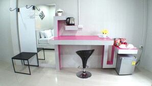 Een kleine kamer met een bureau, een stoel, een tafeltje en een kitchenette.