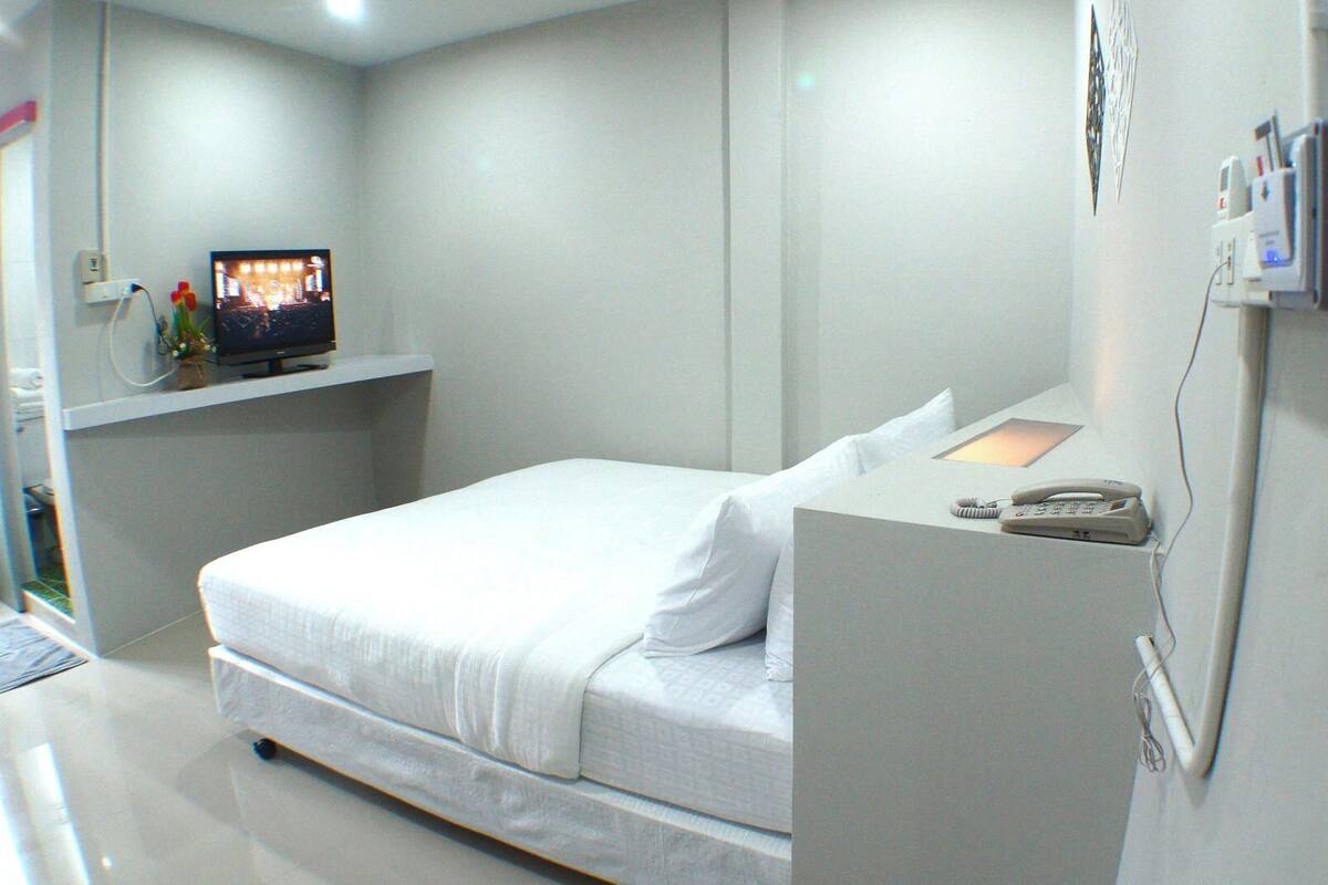 Une chambre d’hôtel avec un lit, un téléviseur posé sur une étagère, un téléphone sur un support et une prise électrique fixée au mur.