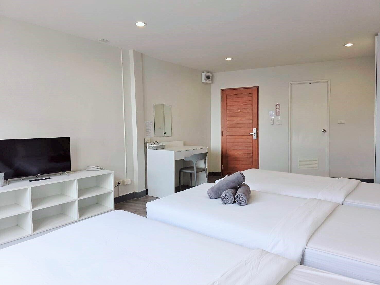 A hotel room with two beds, a TV, a desk, and a wooden door.