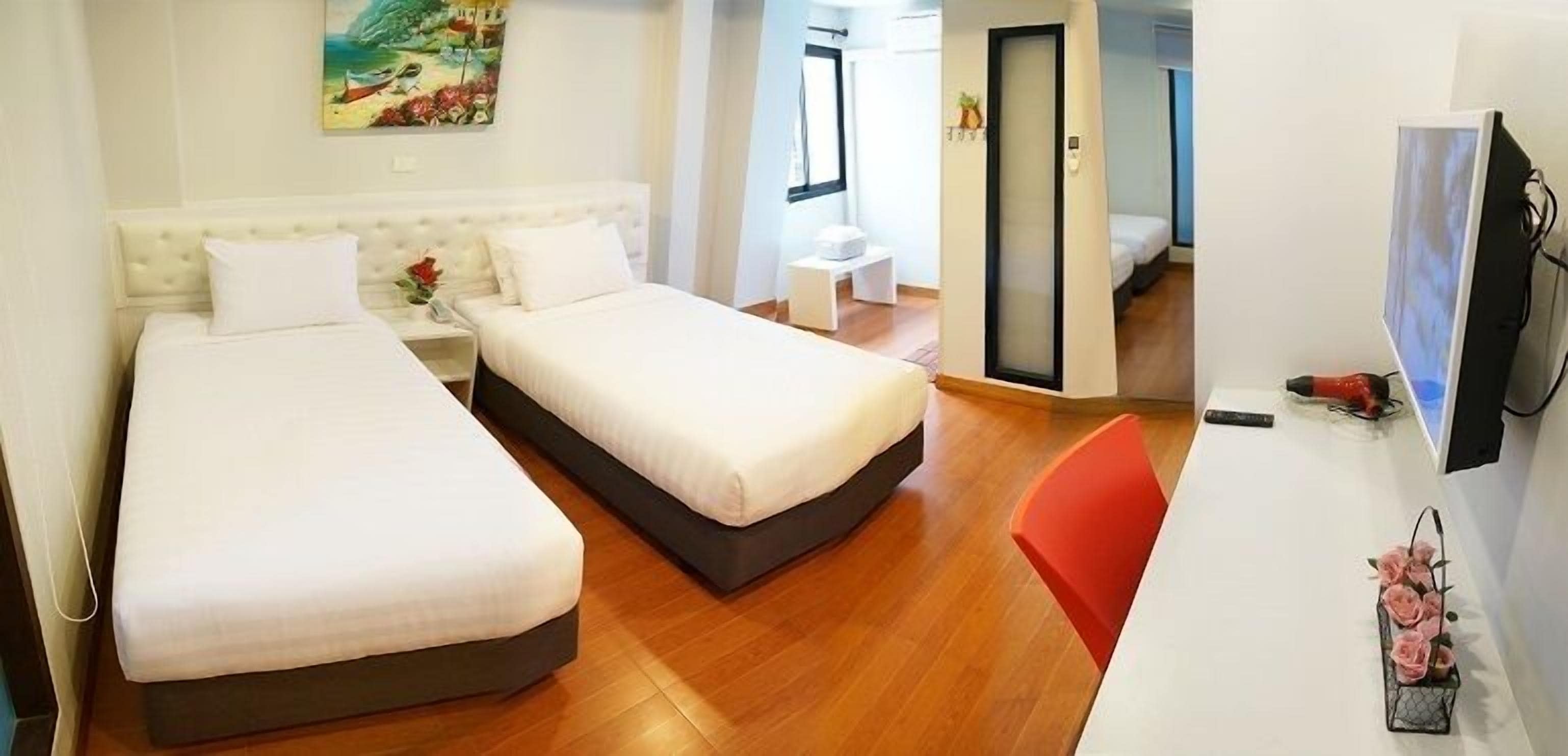 A hotel room with two beds, a small desk, a TV, and a painting on the wall.