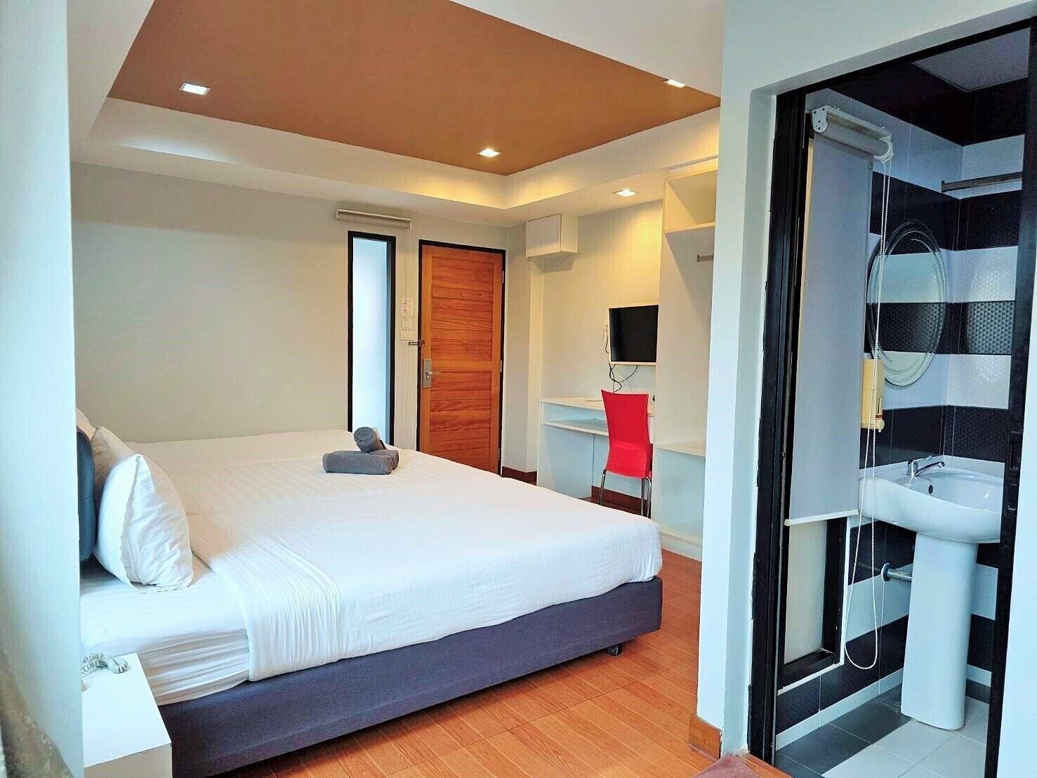 A modern bedroom with a large bed, a wooden door, a desk with a chair, and a bathroom with a sink and shower.