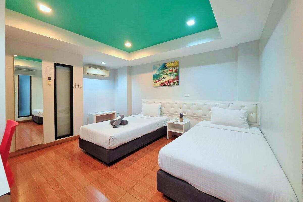 Une chambre d’hôtel avec deux lits, une grande fenêtre, un tableau au mur et un fauteuil rouge.