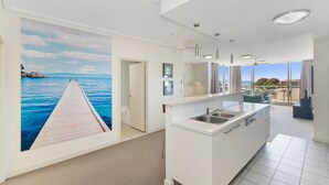 Une cuisine moderne dotée d’un grand îlot central, offrant une vue sur la mer grâce à une fresque murale, et un balcon avec vue sur le paysage.