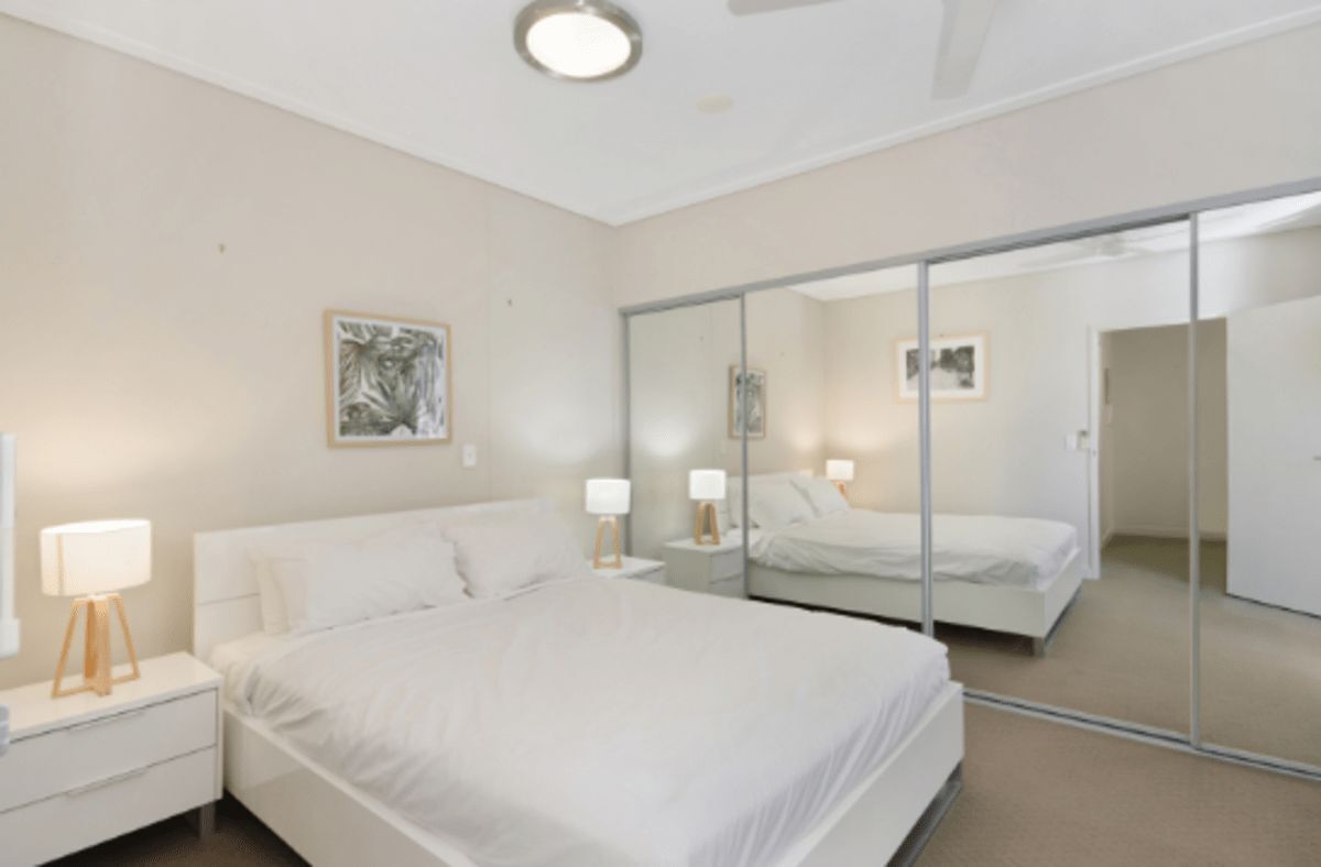 Una camera da letto con un letto, comodini, lampade, uno specchio e un quadro appeso al muro.