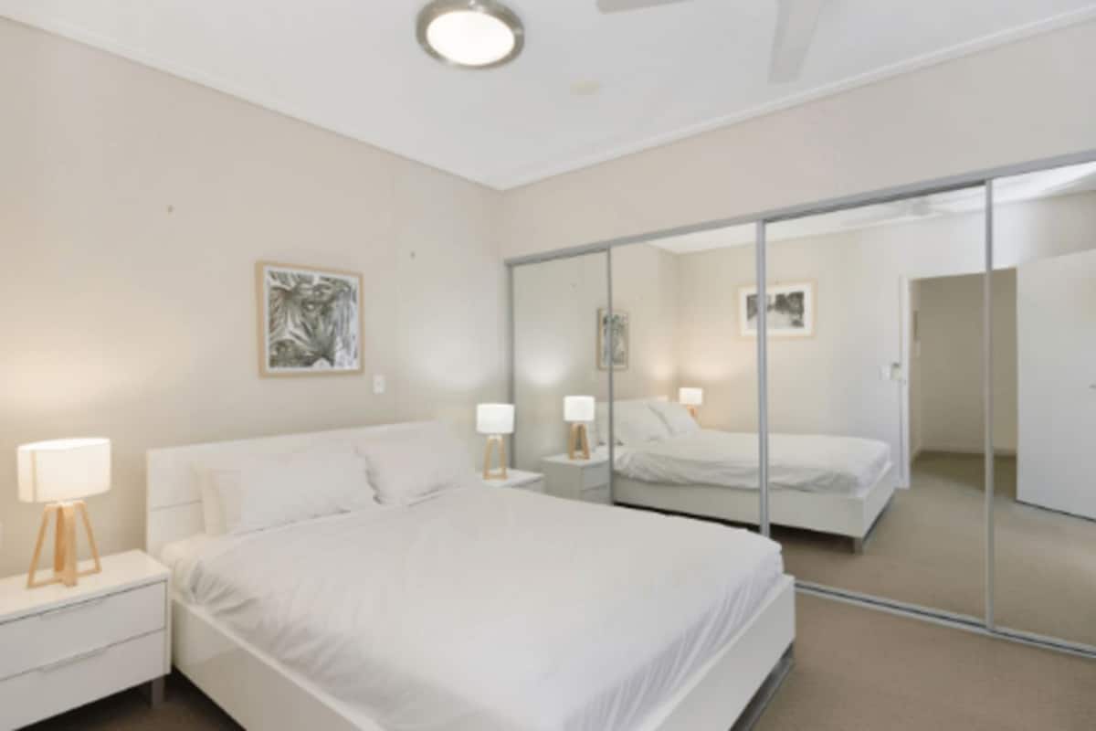 A bedroom with a bed, bedside tables, lamps, a mirror, and a painting on the wall.