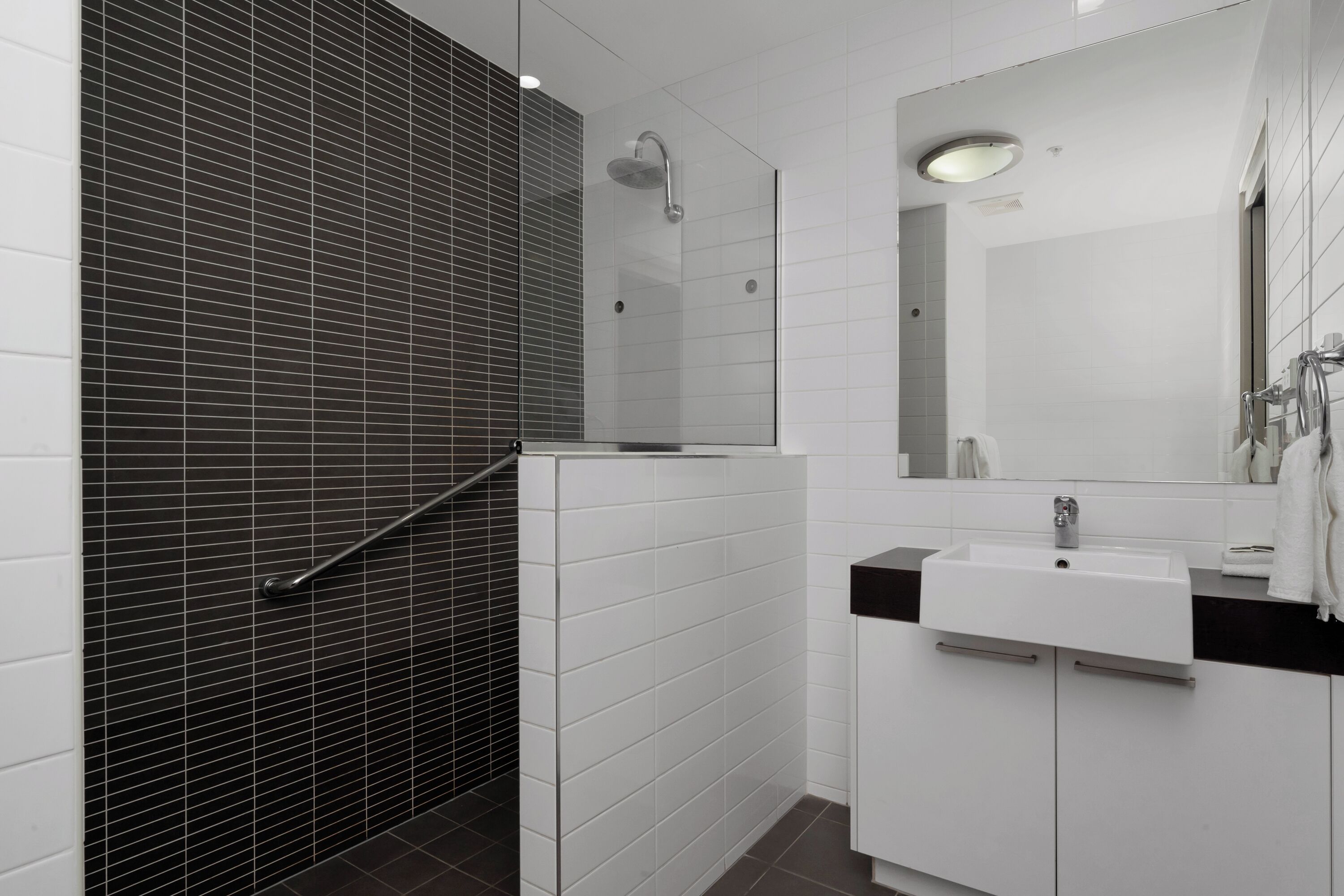 A modern bathroom with a glass shower enclosure, white tiles, and a black countertop sink.