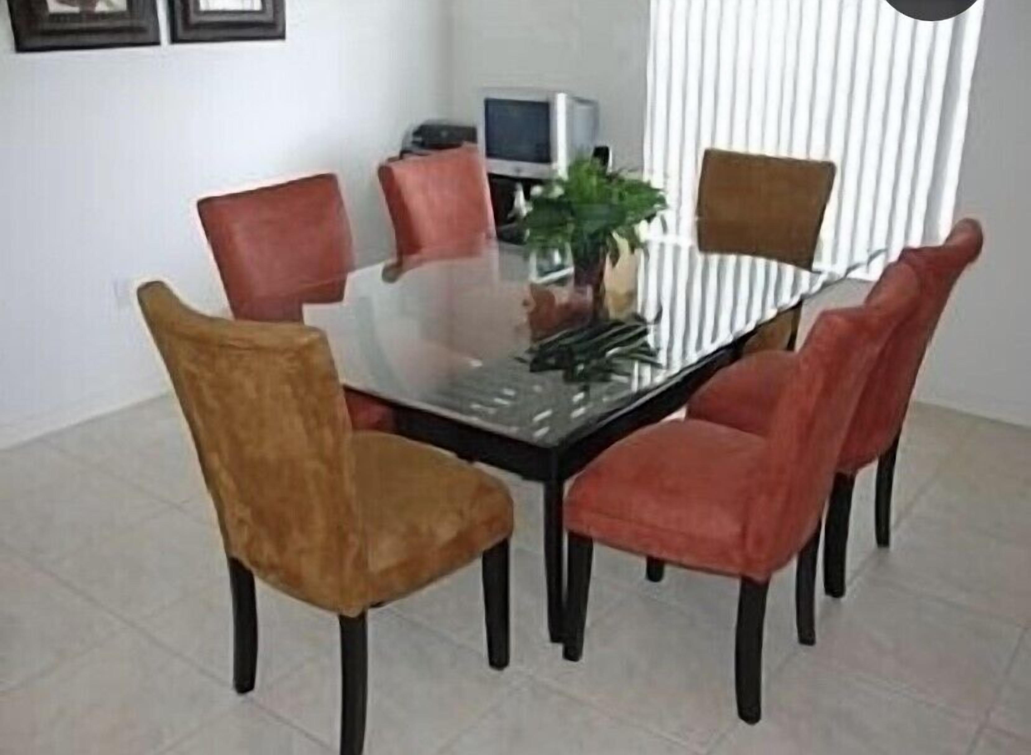 Een eetruimte met een glazen tafel, omringd door zes stoelen, een televisie en een plant.