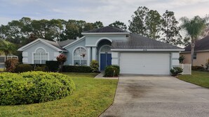 A single-story house with a garage, a front yard with well-maintained grass and shrubs, and a driveway leading to the garage.