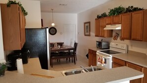 A kitchen with wooden cabinets, a refrigerator, a stove, a sink, and a dining area with chairs and a table.