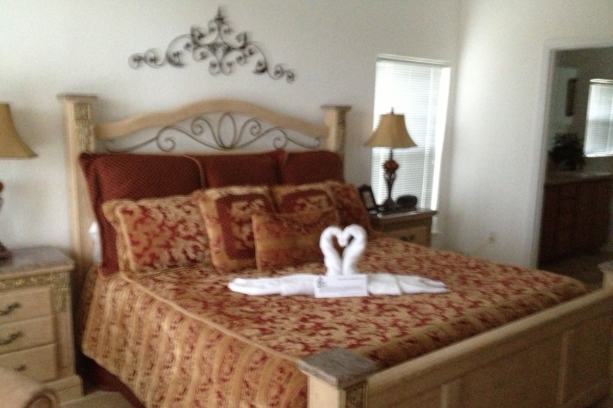 A neatly made bed with a heart-shaped towel arrangement, a wooden headboard, and a floral-patterned bedspread.