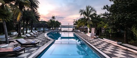 A swimming pool with lounge chairs and palm trees.