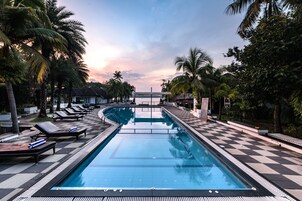 Una piscina con sillones de descanso y palmeras.