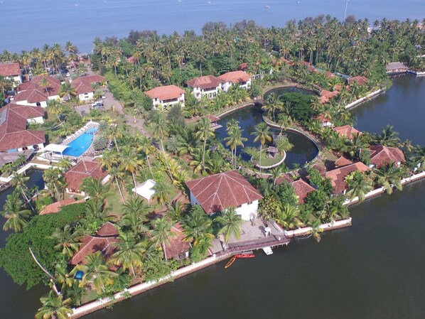 An aerial view of a coastal resort with multiple bungalow-style buildings, a central swimming pool, and a marina.