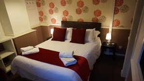 A neatly made bed with red and white bedding, two bedside lamps, and a red throw blanket. - The Boundary Hotel (Leeds)