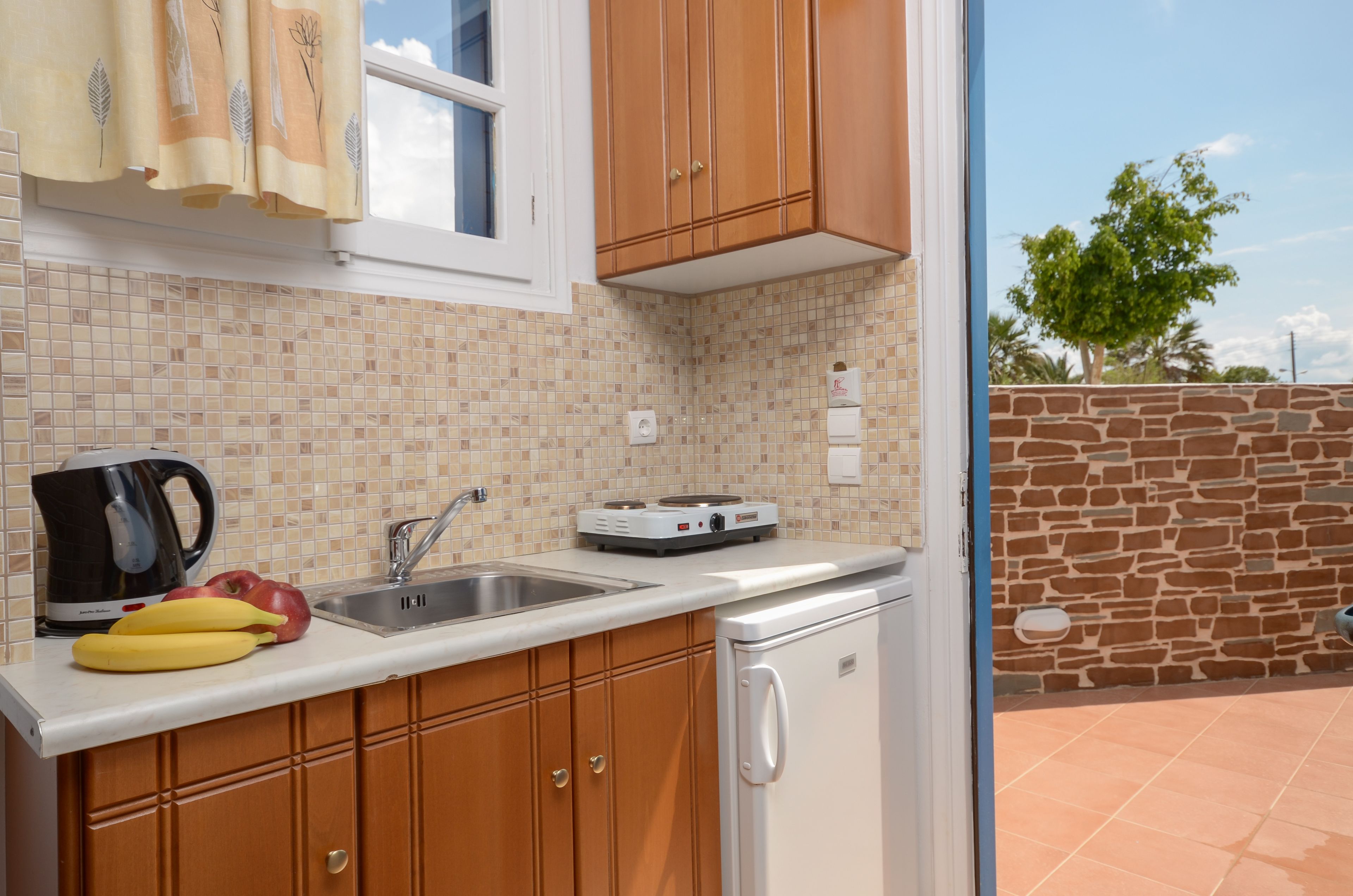 A kitchen with wooden cabinets, a white countertop, a coffee maker, a sink, and a small refrigerator.