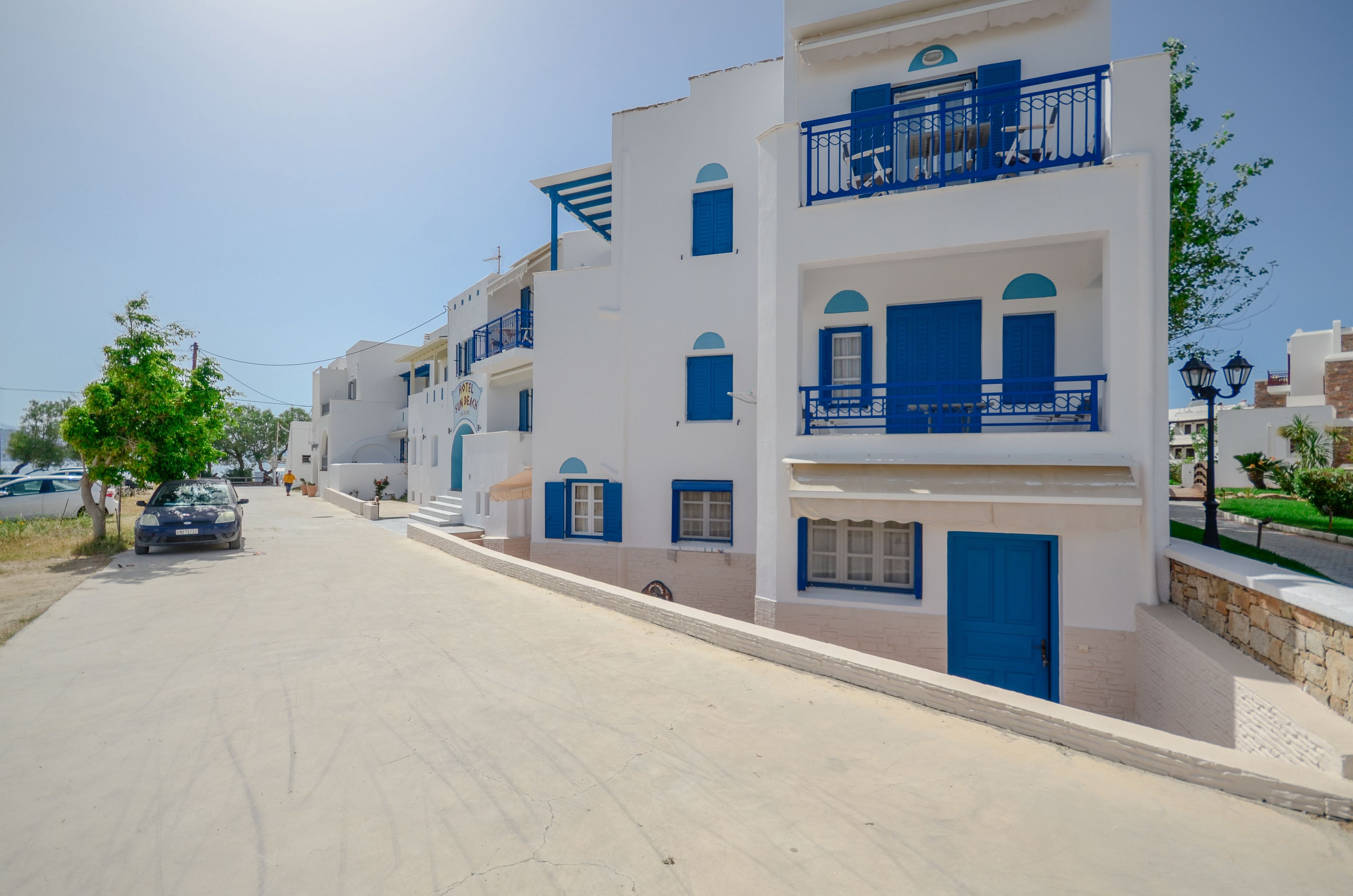 A street lined with white buildings with blue accents, featuring balconies and doors.