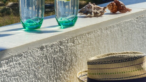 Two glasses of blue liquid with lemon slices on a balcony overlooking a beach with a hat and seashells. - Sun Beach Hotel (Naxos)