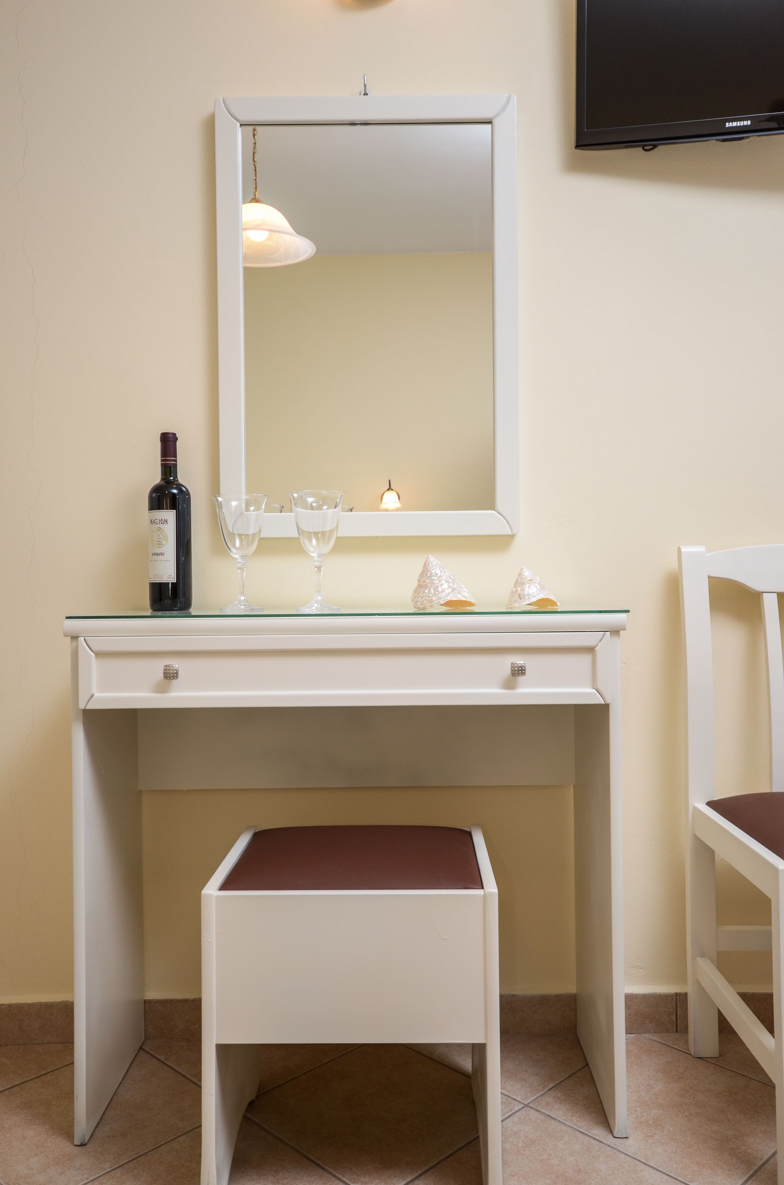 A white desk with a mirror, a bottle of wine, and two glasses.