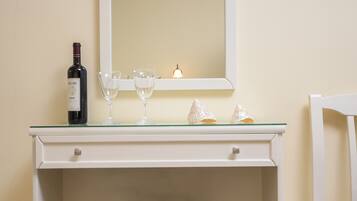 A white desk with a mirror, a bottle of wine, and two glasses.