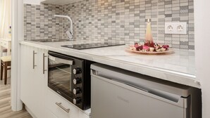 A modern kitchen with white cabinetry, a tiled backsplash, a built-in oven, and a refrigerator. - Sun Beach Hotel (Naxos)