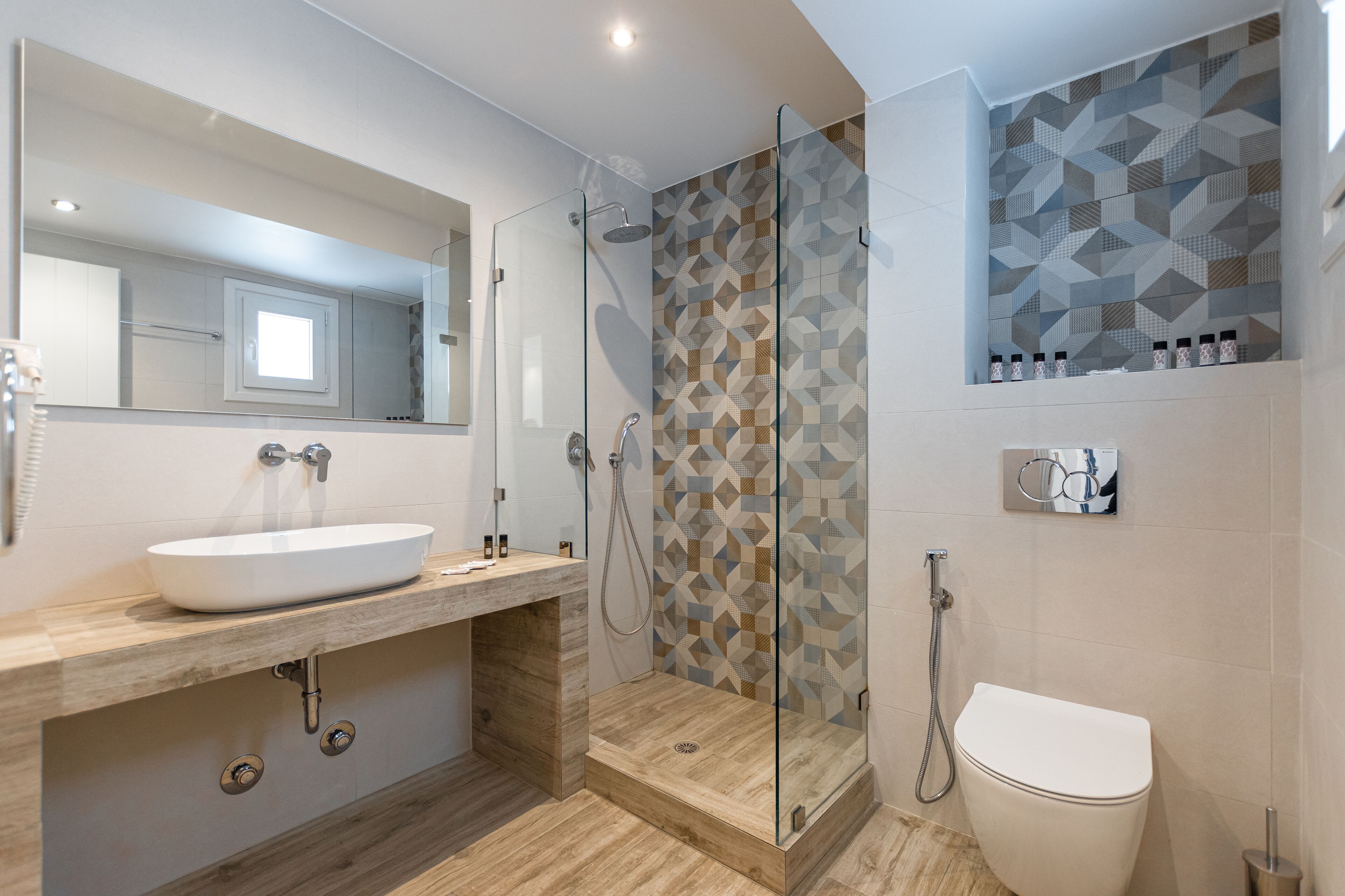 Een moderne badkamer met een douche met glazen wand, een wit wastafelmeubel en een betegelde douchewand.