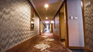 Un pasillo de hotel con alfombra estampada, paneles de madera y una larga extensión con puertas a ambos lados.