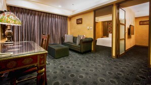 Habitación de hotel con una mesa de vidrio, un sofá con cojines estampados, una alfombra con diseño y una puerta que da al baño.