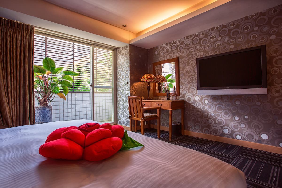 A hotel room with a bed, a desk, a chair, a TV, and a window with blinds.