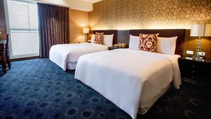 Habitación de hotel con dos camas, un ventanal grande con cortinas, pared con estampado y alfombra oscura.