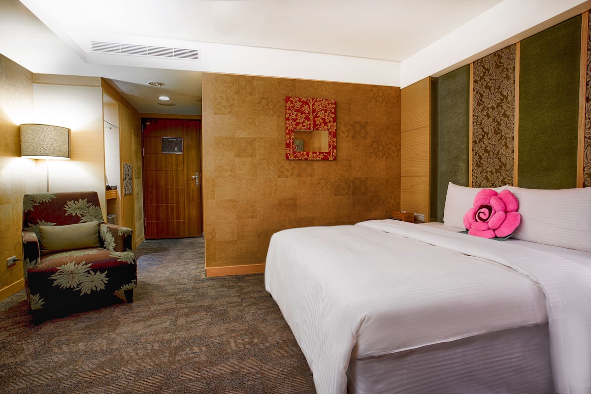 A hotel room with a large bed, a chair, a lamp, and a door.