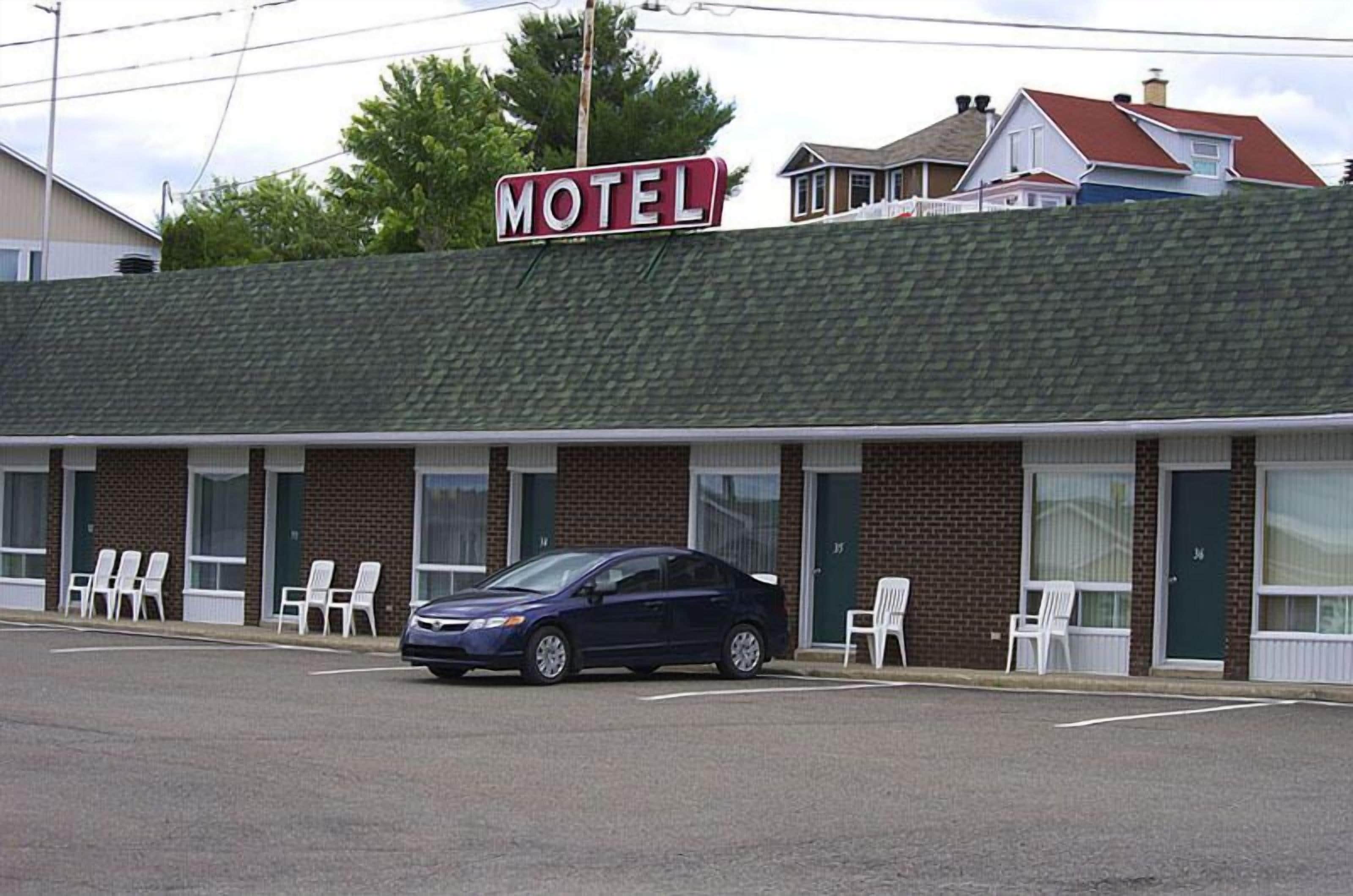 A motel with a 'MOTEL' sign, a parking lot, and a row of white chairs outside.