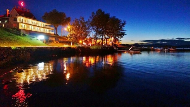 A waterfront property with a large house, trees, and a calm body of water reflecting lights. - Motel Royal (Temiscouata-sur-le-Lac)