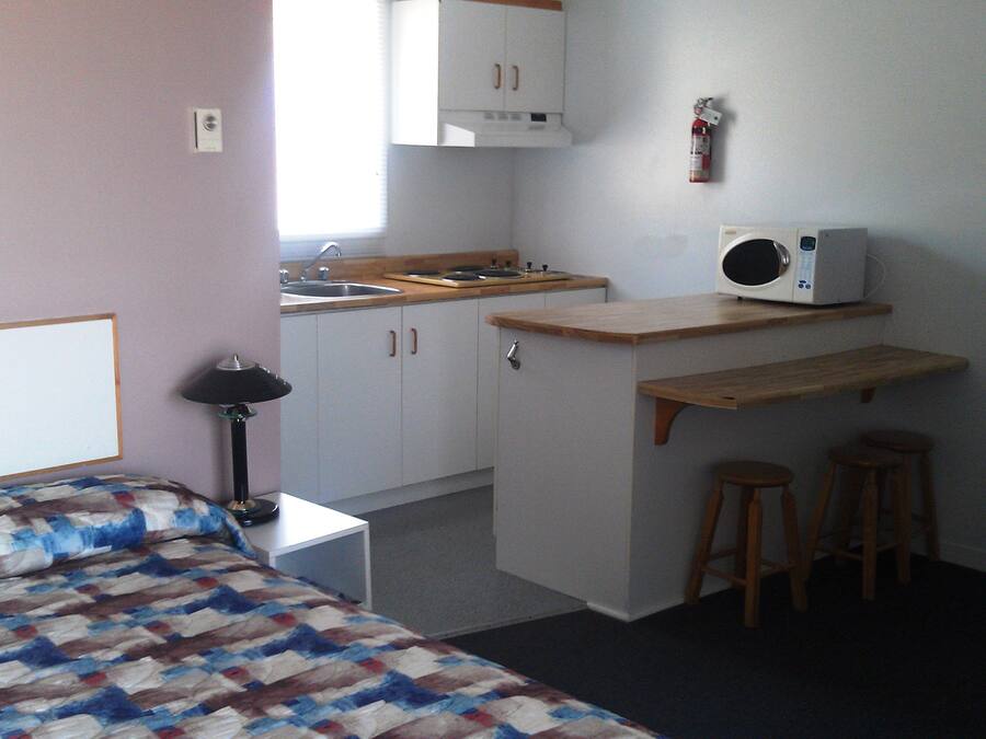 Habitación compacta con cama, una kitchenette pequeña, microondas y extintor.