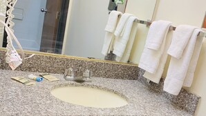 Ein Badezimmer mit einer Granit-Arbeitsplatte, einem Waschbecken, einem Spiegel und einem Handtuchhalter mit weißen Handtüchern.