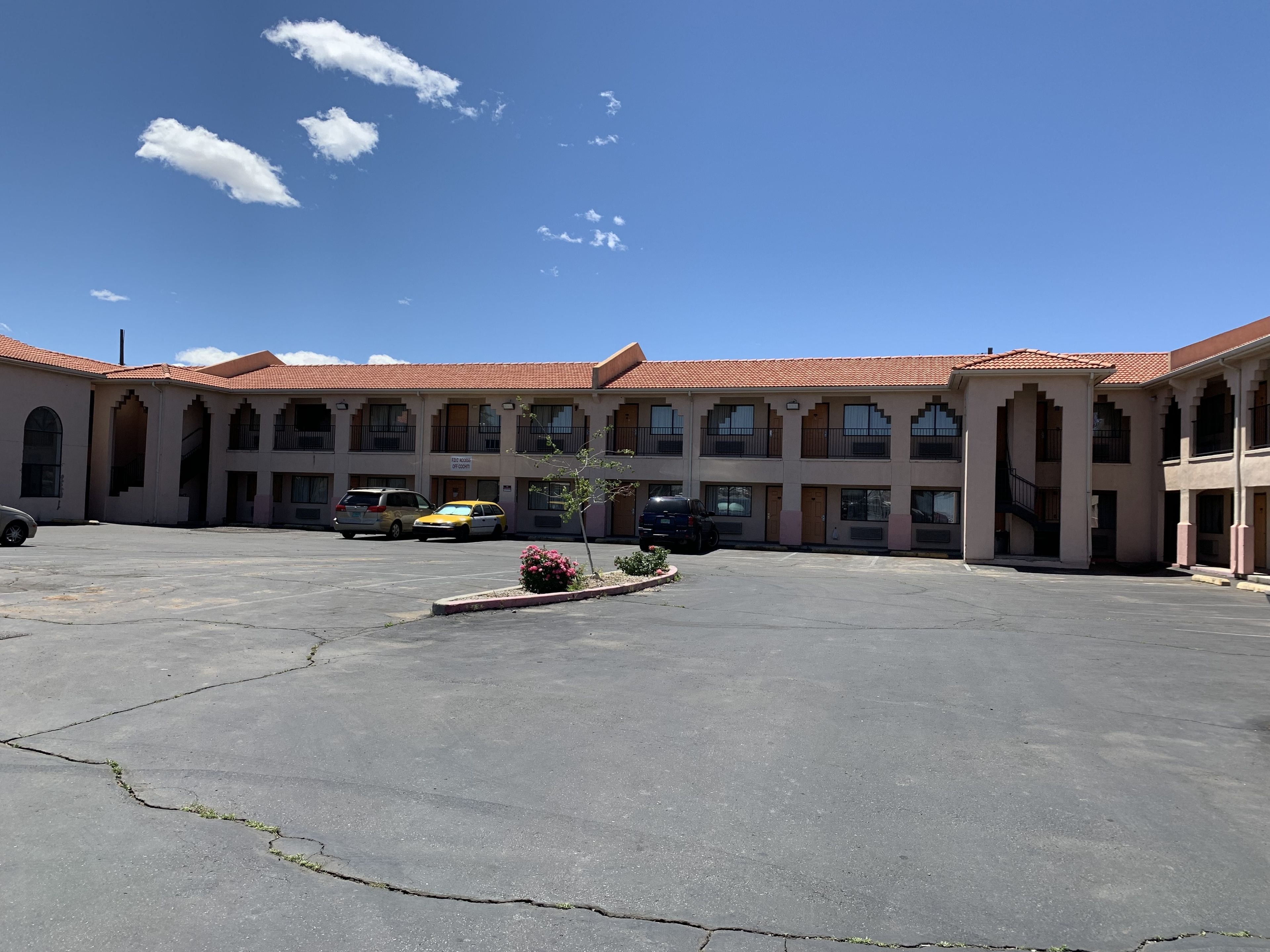 A building with a red-tiled roof, multiple balconies, and a parking lot with several cars.