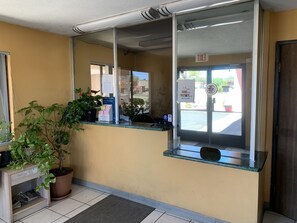 A hotel reception area with a counter, potted plants, and a glass door with an exit sign. - Luxury Inn (Albuquerque)