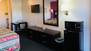 Ein Hotelzimmer mit Bett, Schreibtisch, Kommode, Fernseher, Lampe und einer Mikrowelle.