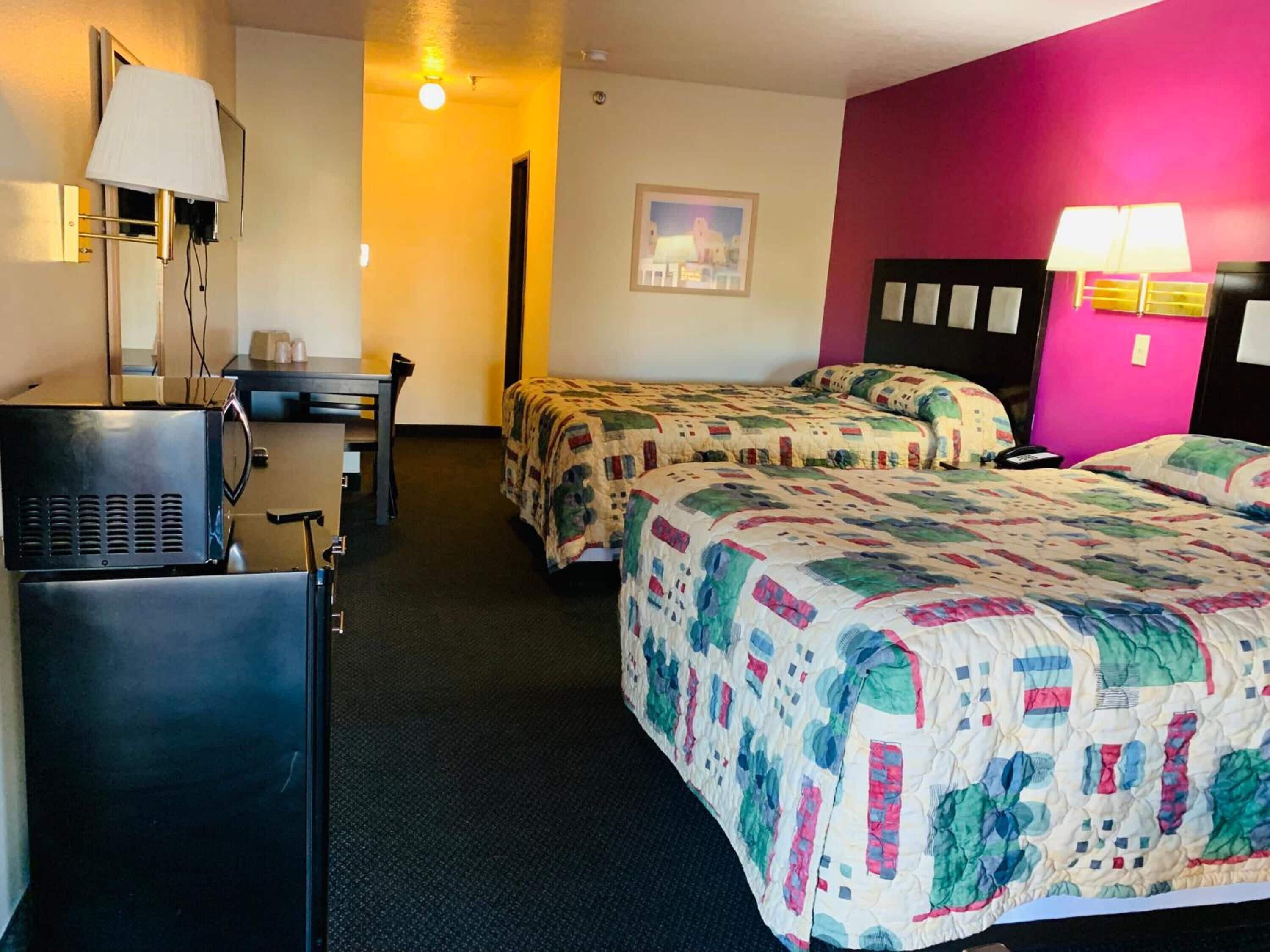 A hotel room with two beds, a desk, a chair, a lamp, and a picture on the wall.