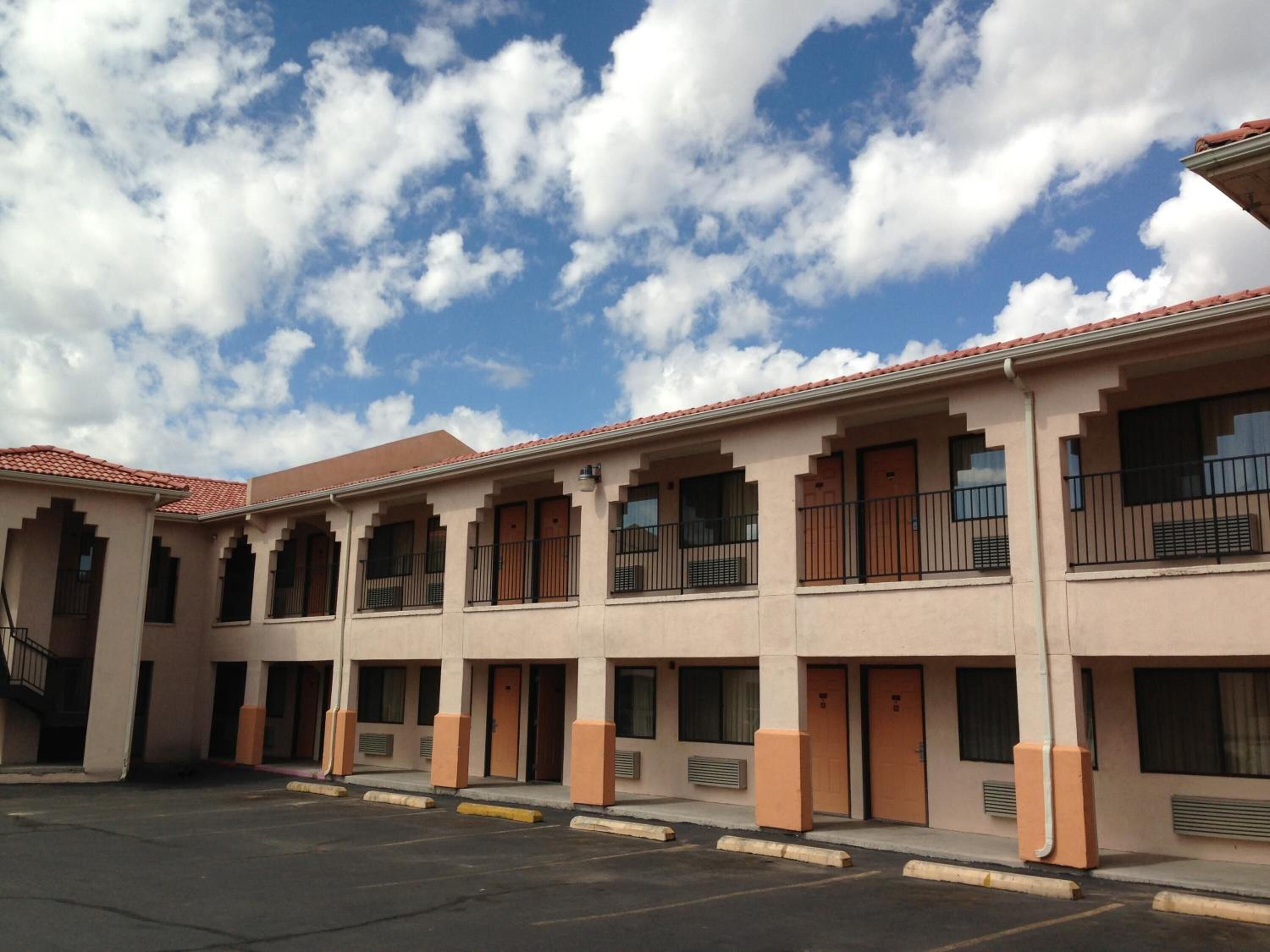 Um motel com uma fileira de quartos, cada um com uma varanda e uma janela.