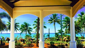 A covered outdoor area with white columns and arches, palm trees, and a view of the ocean. - Amoa Resort Savaii (Tuasivi)