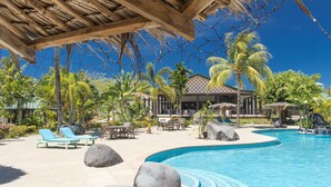 A resort pool area with lounge chairs, a wooden pergola, palm trees, and a building with a thatched roof. - Amoa Resort Savaii (Tuasivi)