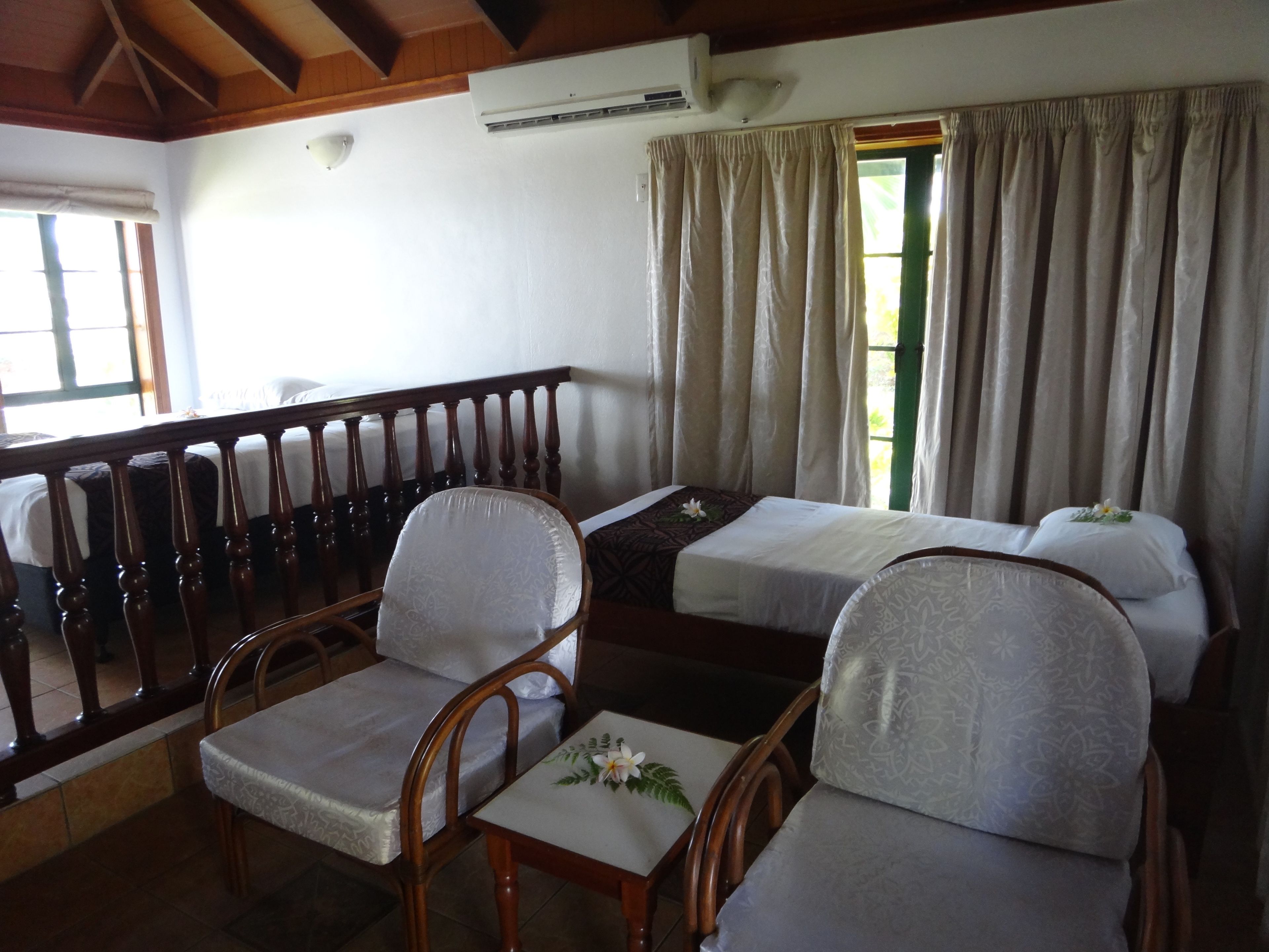 A hotel room with two single beds, a wooden chair, a small table, and a balcony with a railing.