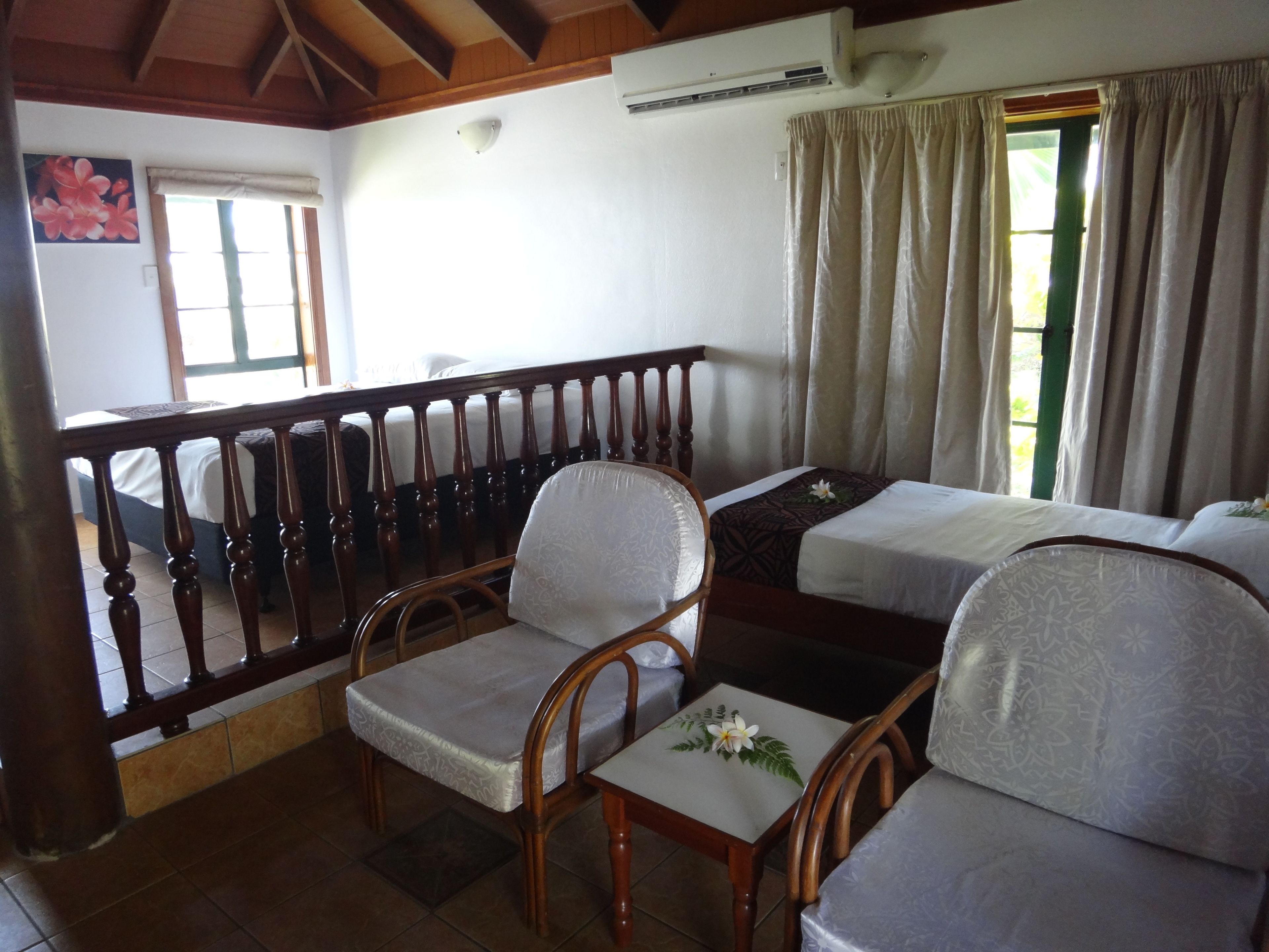 A room with two single beds, a wooden chair, a small table, and a balcony with a railing.