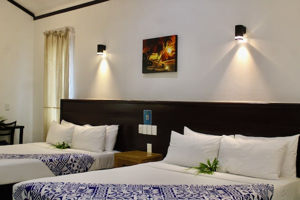 Habitación de hotel con dos camas, un cuadro en la pared y una mesita de noche con una lámpara.